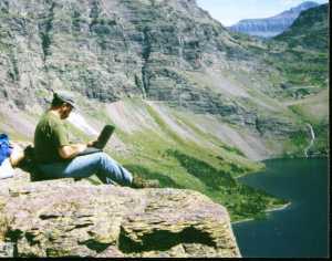 Photo of Bill Binder sitting on a cliff,, typing on a laptop
